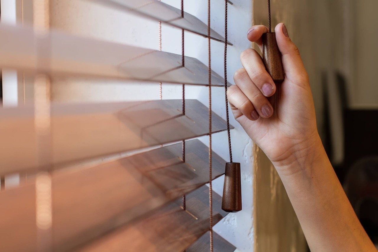  Woman’s hand adjusting wooden window blinds near Silver Spring, MD.